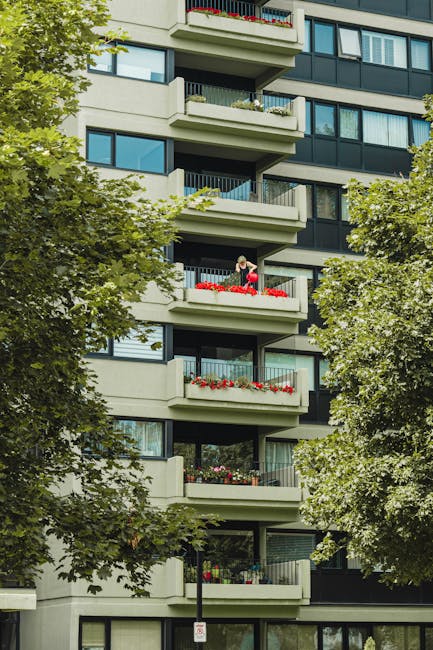 Exterior view of a three-story brick residential building in Churchill Gardens estate with a sloped tiled roof and multiple black-framed windows. In front, there is a pathway lined with well-maintaine